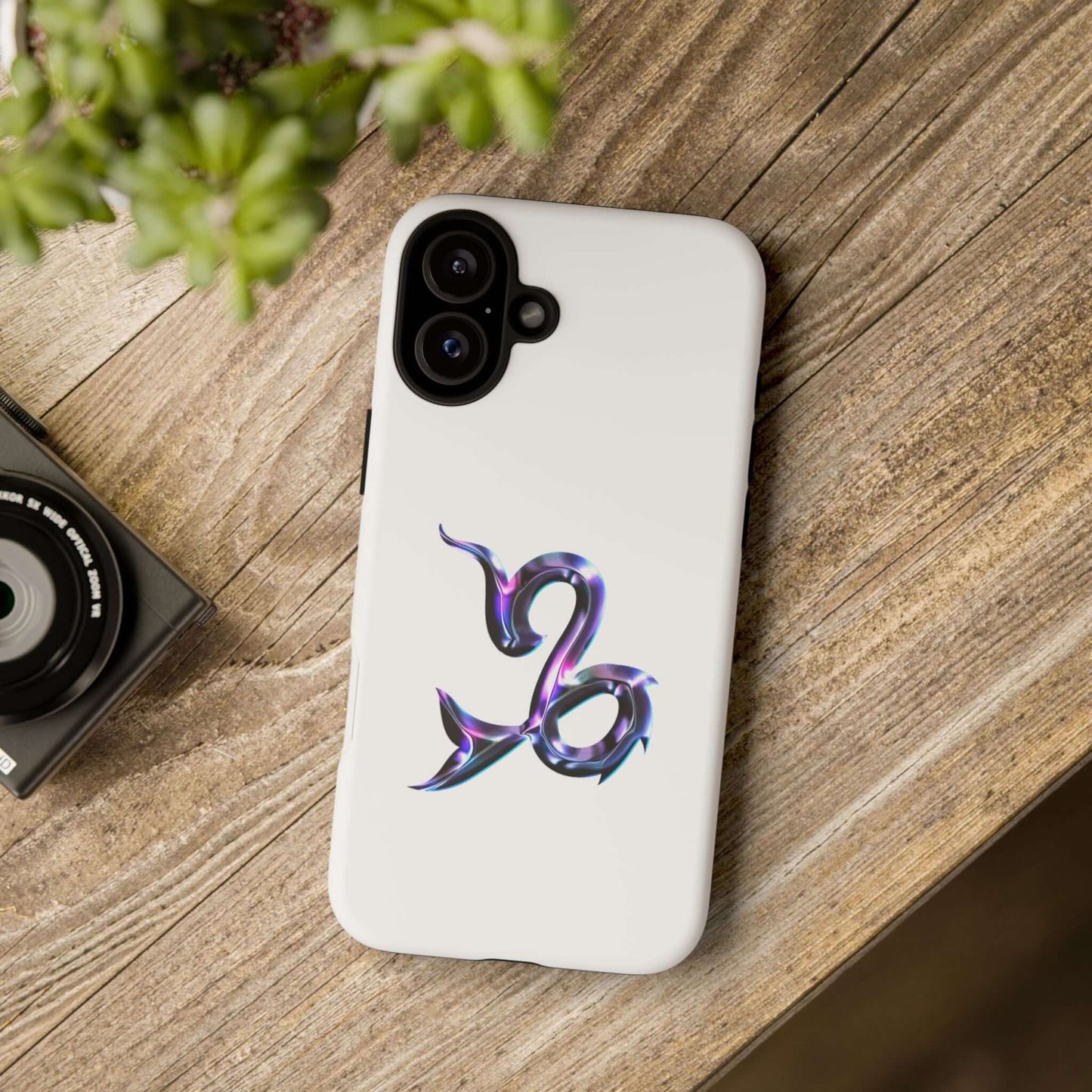 Personalized Capricorn zodiac phone case design on a wooden surface with camera and plant.