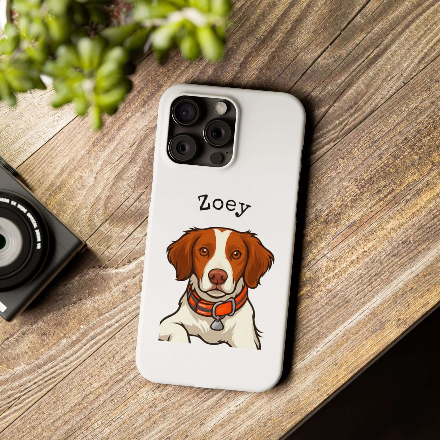 Custom cartoon phone case featuring a dog named Zoey, on a wooden surface with camera and greenery.