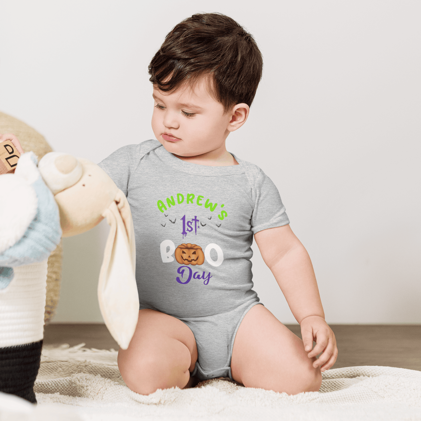 Baby in personalized gray bodysuit celebrating 1st Halloween with playful pumpkin design and colorful text.