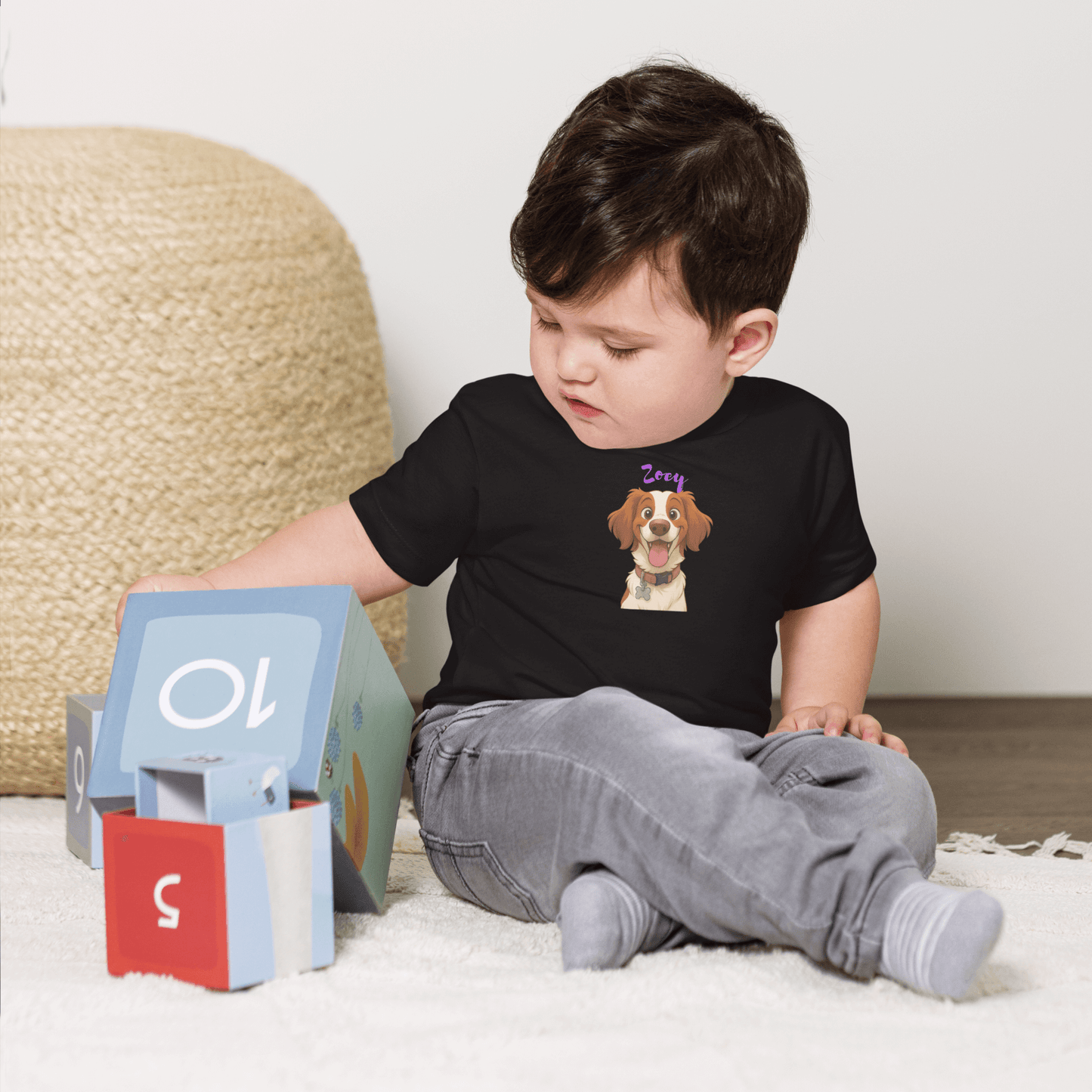 Toddler wearing a custom cartoon pet baby shirt featuring a dog, engaged with colorful blocks on a cozy floor.