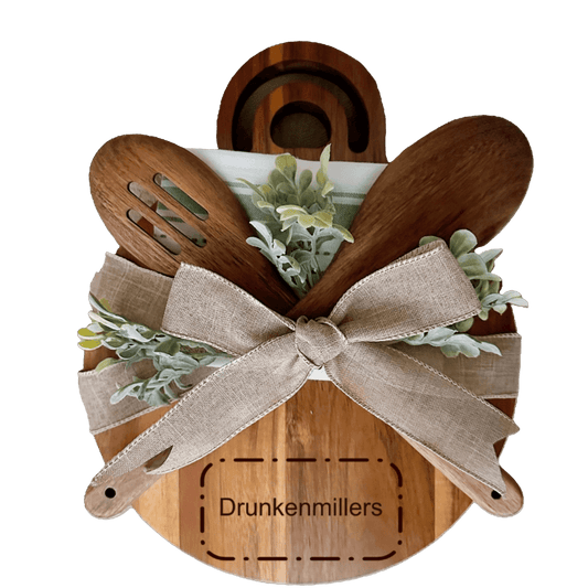 Personalized wooden cheese board with kitchen utensils and greenery, engraved with 'Drunkenmillers'.