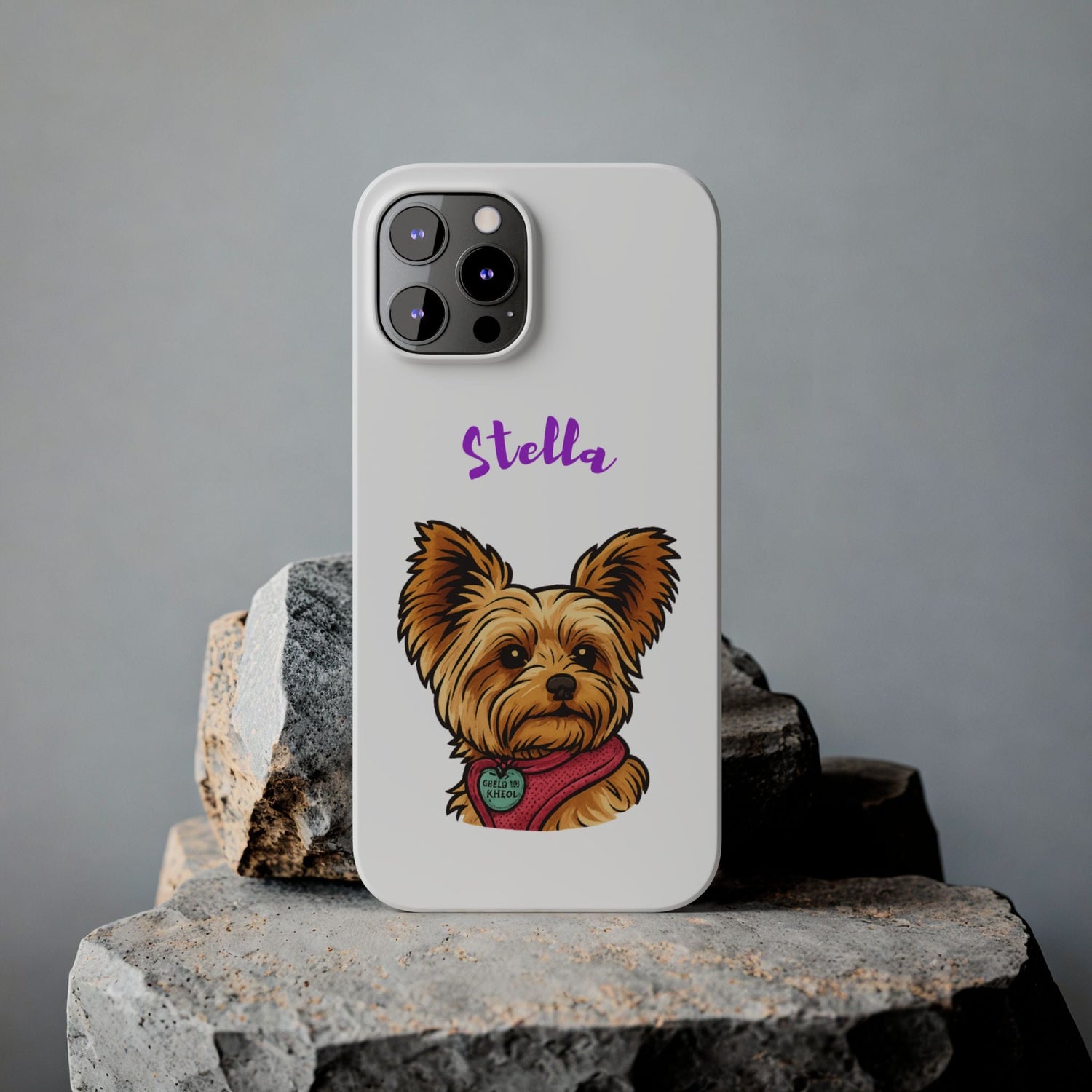 Cartoon illustration of a Yorkshire Terrier named Stella on a phone case, set against a rocky background.