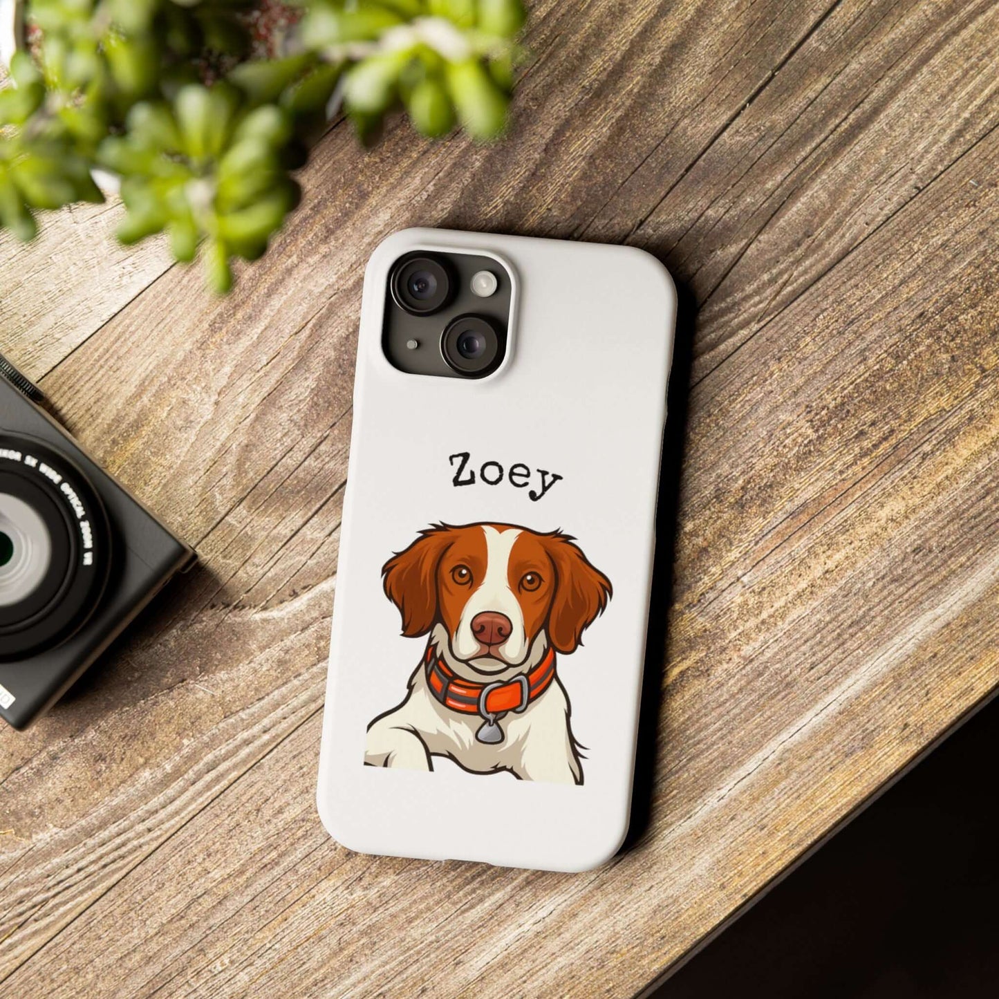 Custom cartoon phone case featuring a dog illustration named Zoey, on a wooden surface with a camera.
