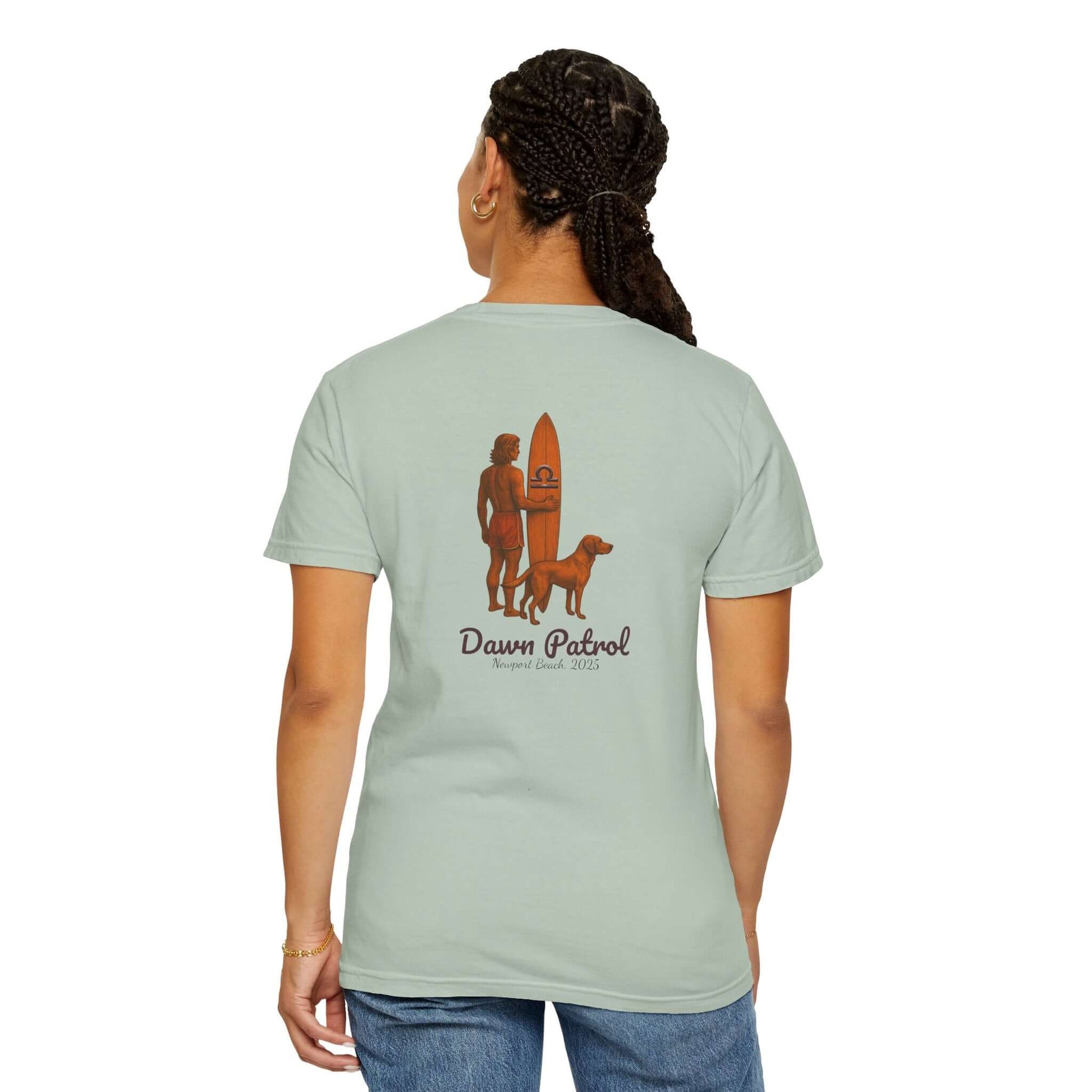 Back view of a woman wearing a mint green t-shirt with a surf and dog design, labeled 'Dawn Patrol'.