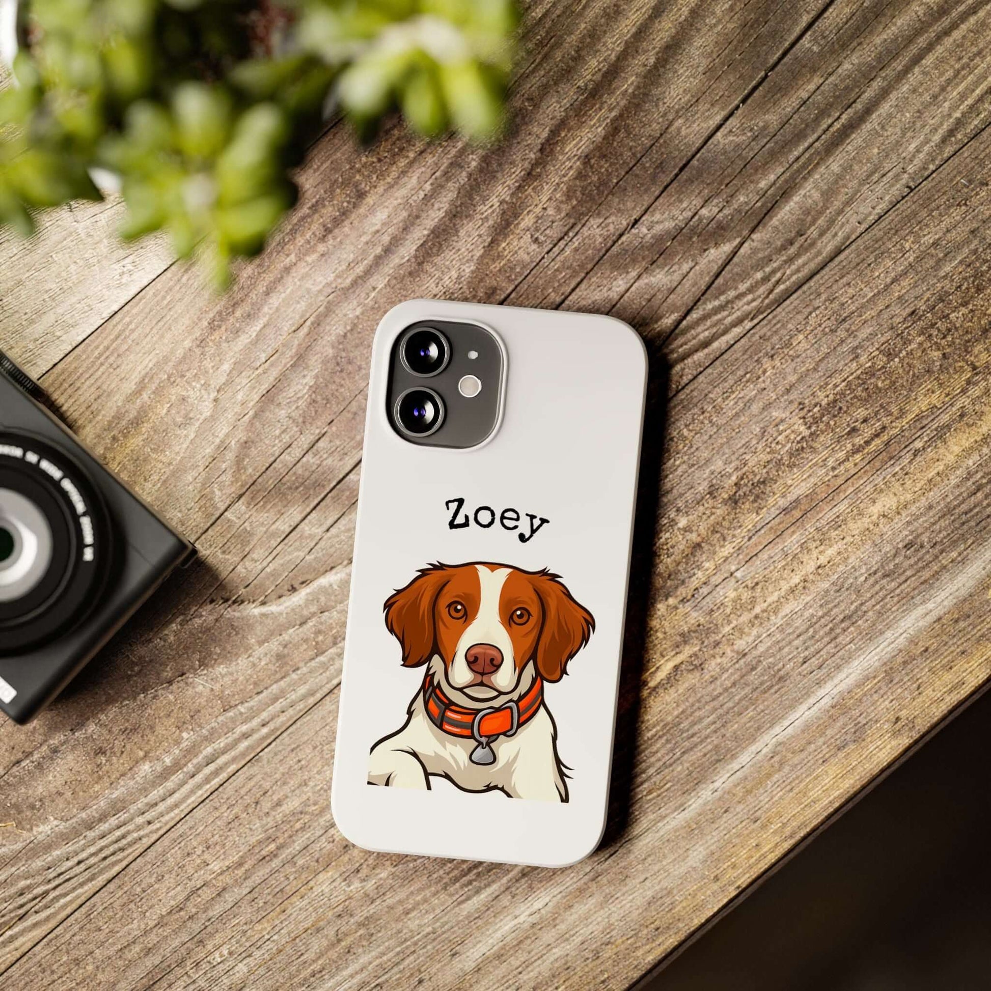 Custom cartoon dog phone case with pet portrait titled 'Zoey', placed on a wooden table beside a camera.