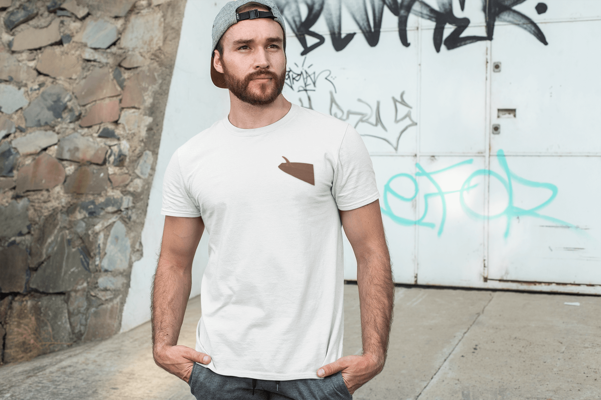 Man wearing a white personalized t-shirt with a brown pocket design, standing against a graffiti wall.