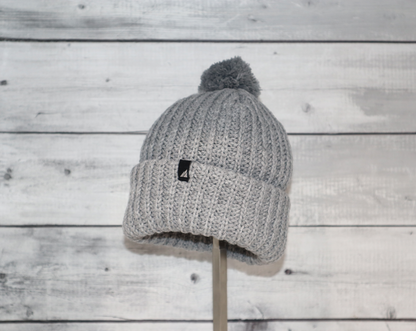 Child Acrylic Ribbed Cuff Hat with Pom – Cozy, Playful, Purposeful on wooden background.