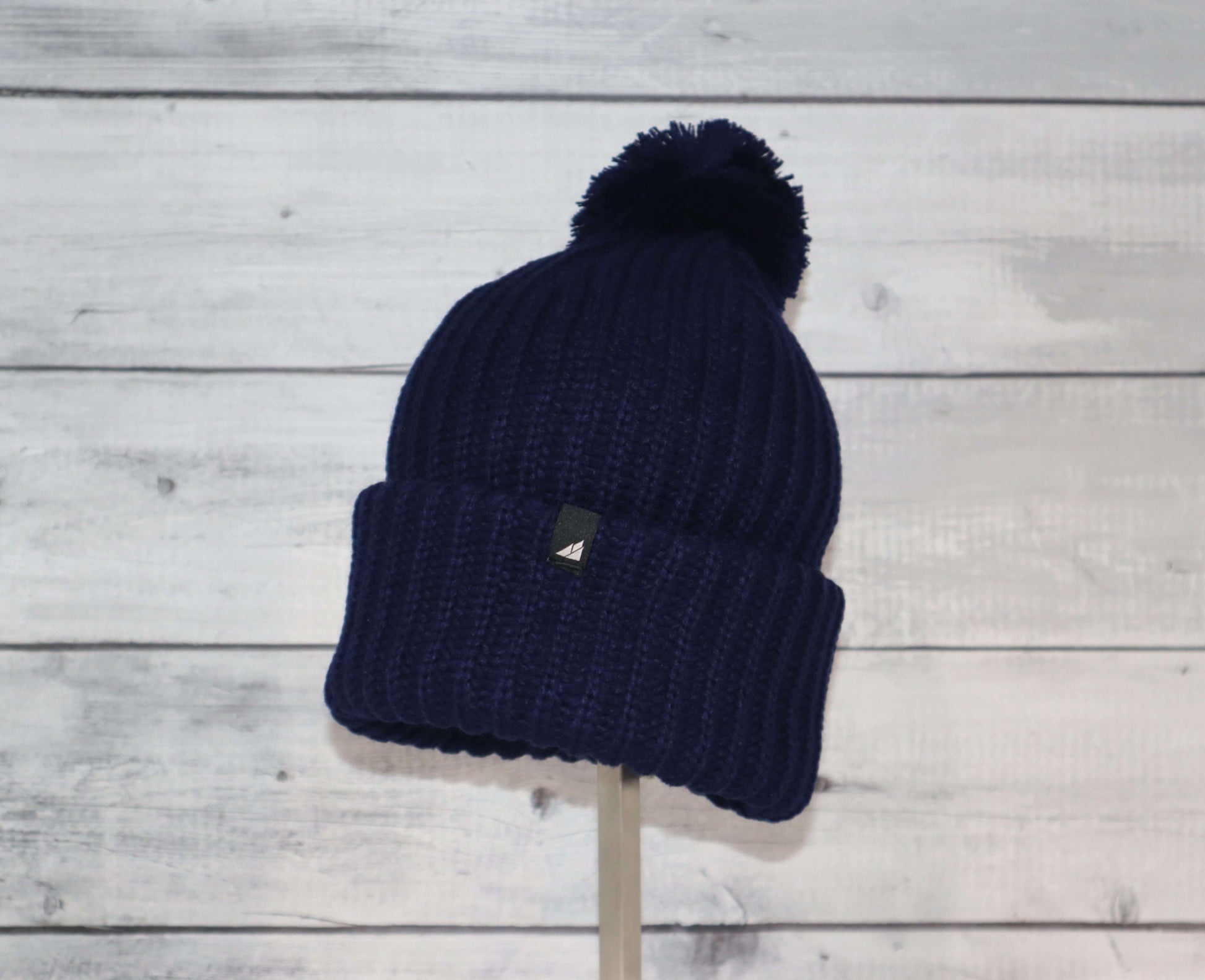 Child Acrylic Ribbed Cuff Hat with Pom – Cozy, Playful, Purposeful on display with a navy color.