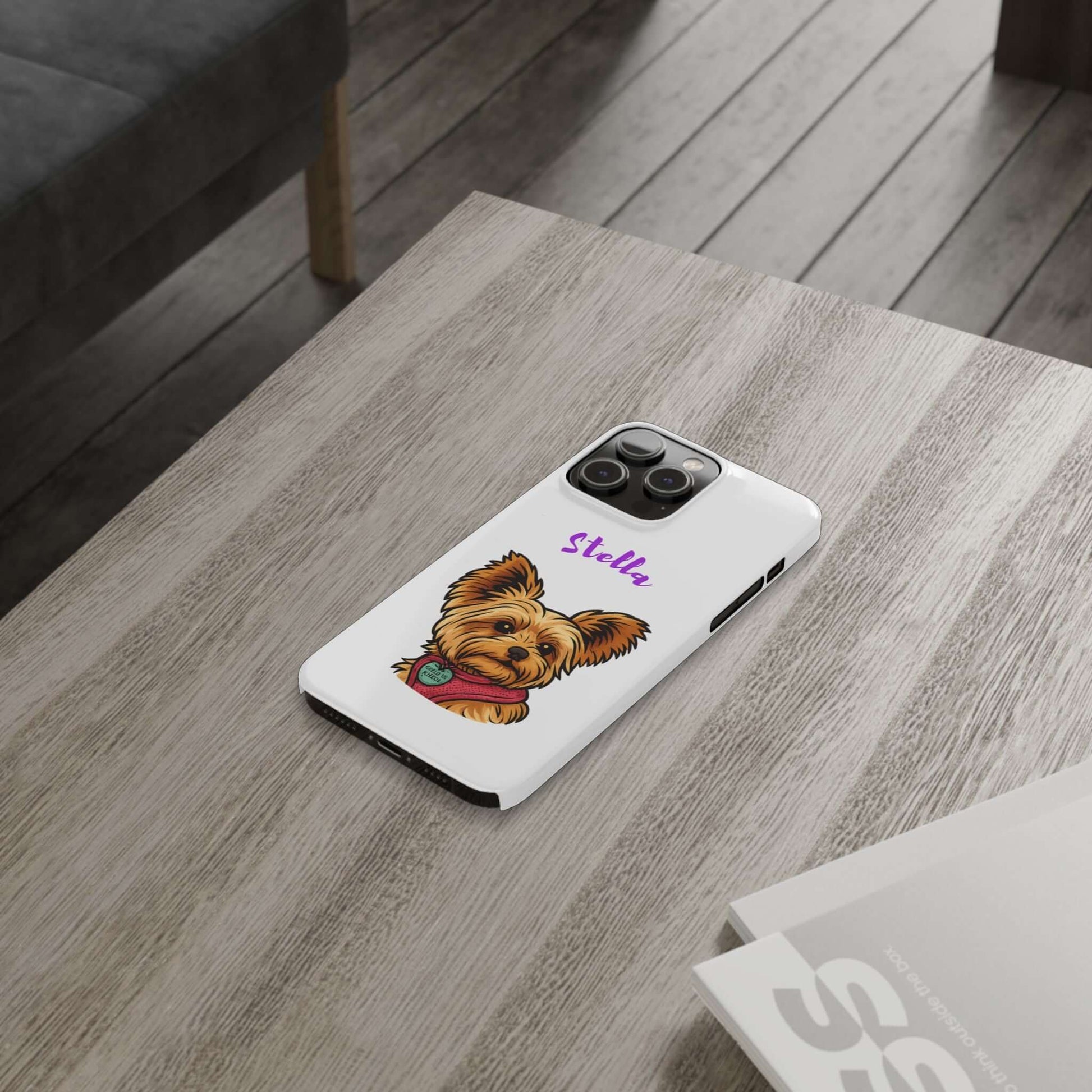 Custom dog cartoon phone case with a Yorkie design and name Stella, placed on a wooden table.