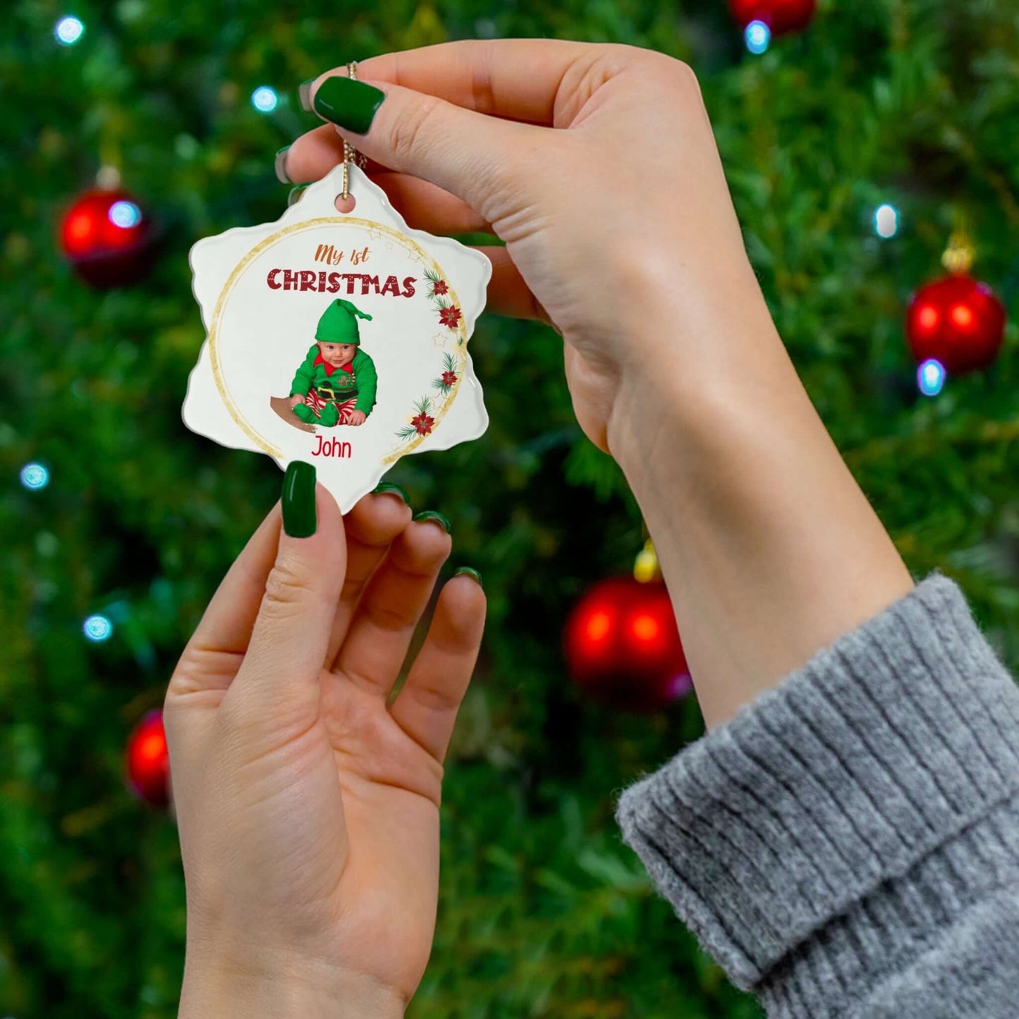 My 1st Christmas Ornament – Custom Photo in 4 Shapes held by hands in front of a festive tree.