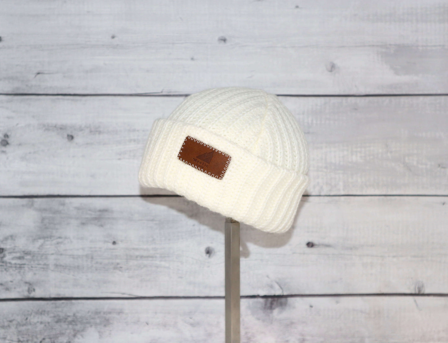 Infant Acrylic Ribbed Cuff Hat – Soft, Stretchy & Purposeful on a display stand against a rustic wooden background.