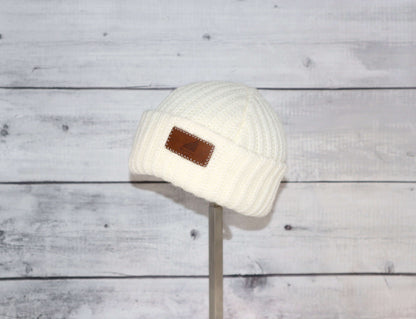 Infant Acrylic Ribbed Cuff Hat – Soft, Stretchy & Purposeful on a display stand against a rustic wooden background.