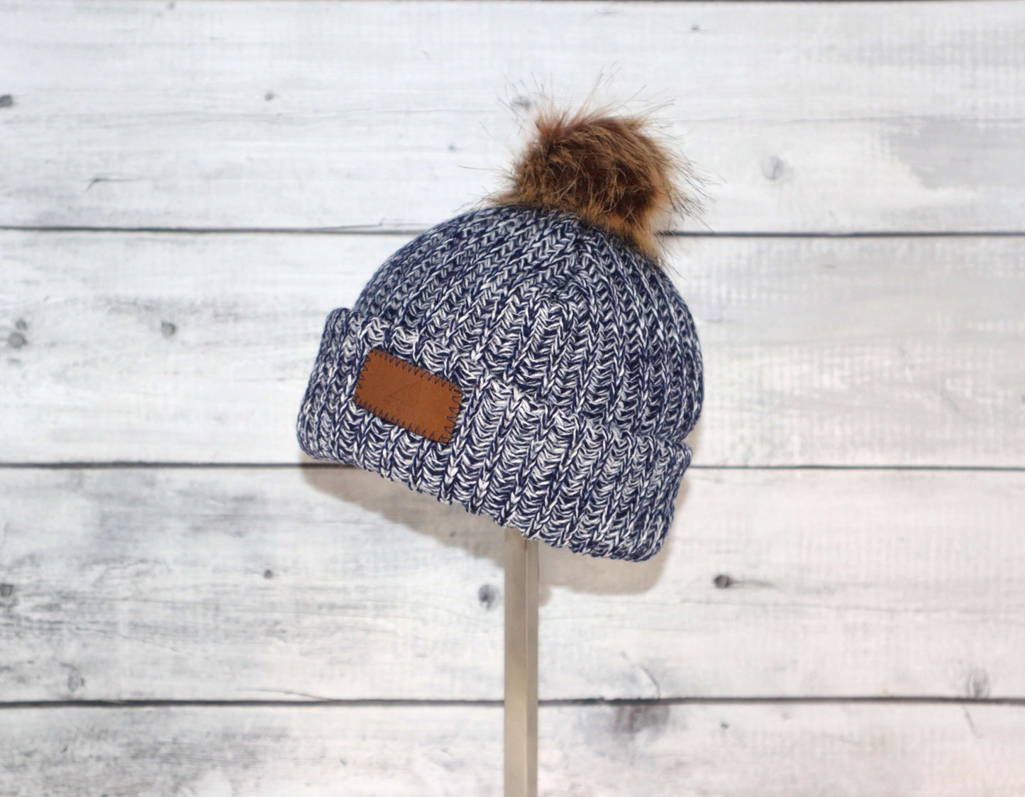 Infant Acrylic Ribbed Cuff with Pom Hat – Cozy & Purposeful displayed on a stand against a rustic wooden background.