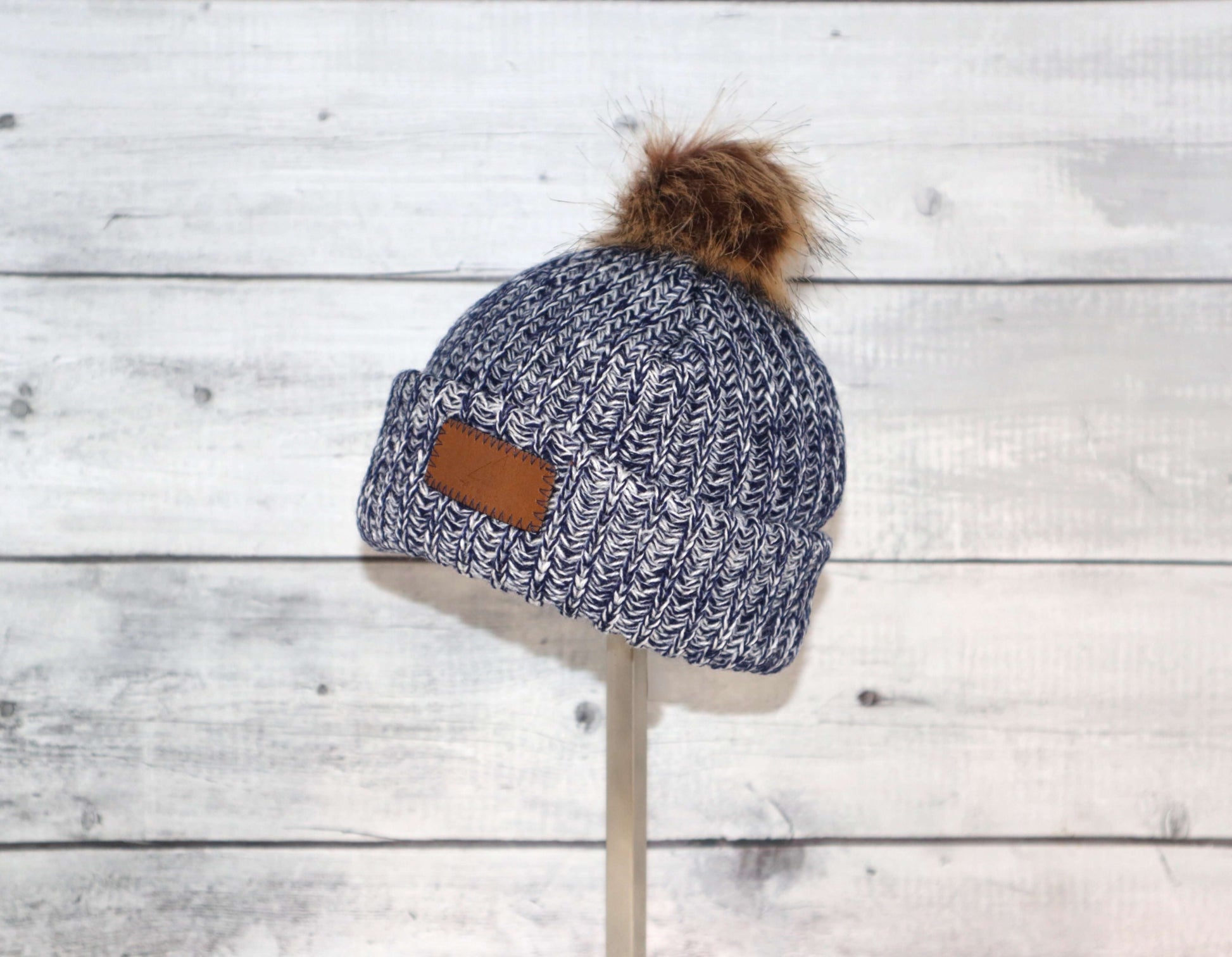 Infant Acrylic Ribbed Cuff with Pom Hat – Cozy & Purposeful displayed on a stand against a rustic wooden background.