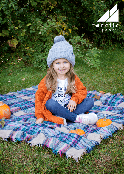 Child Acrylic Ribbed Cuff Hat with Pom – Cozy, Playful, Purposeful worn by a smiling girl outdoors.