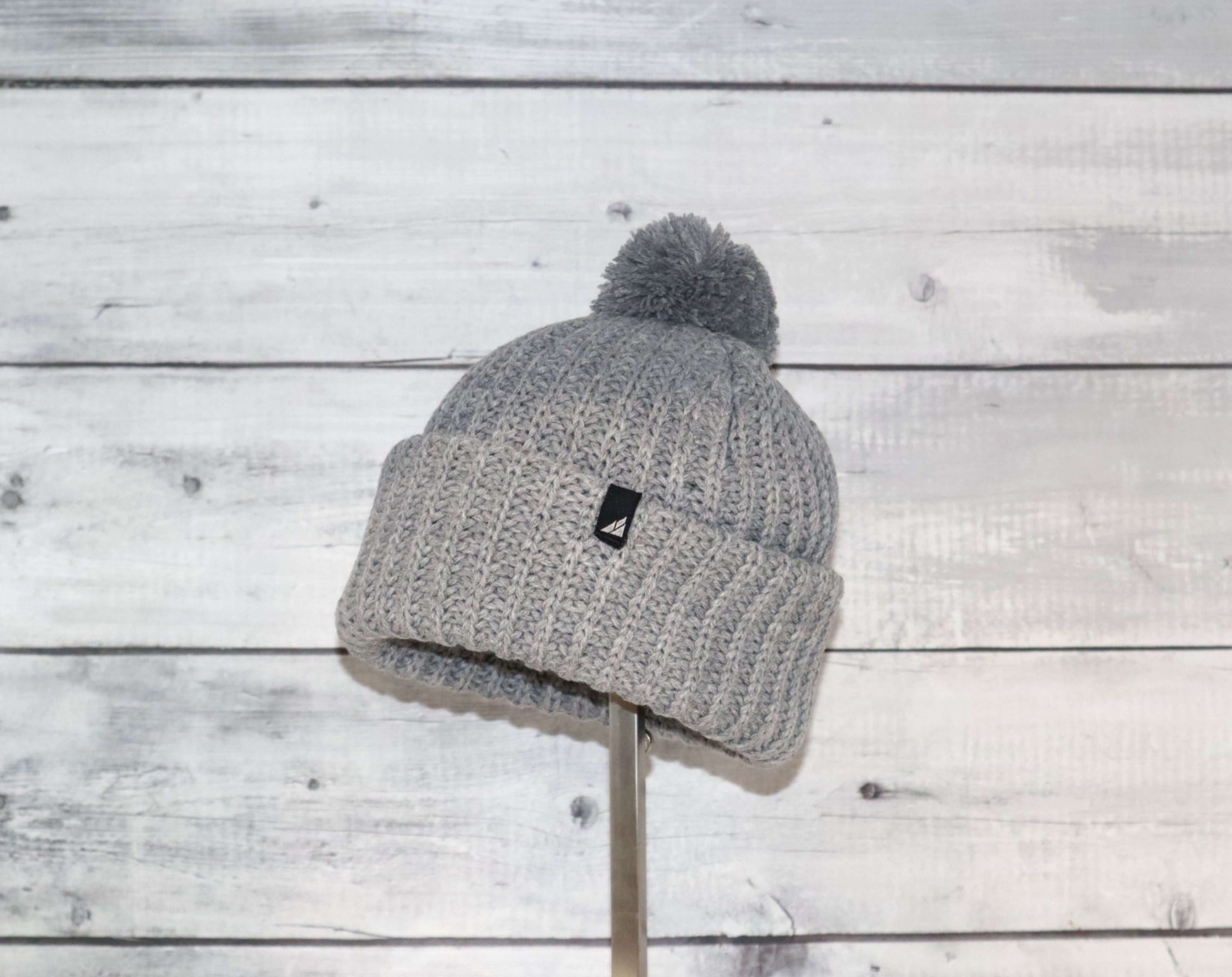 Toddler Acrylic Ribbed Cuff with Pom Hat – Cozy & Purposeful displayed on a stand against a wooden backdrop.