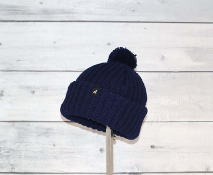 Toddler Acrylic Ribbed Cuff with Pom Hat – Cozy & Purposeful on display against a rustic wooden background.