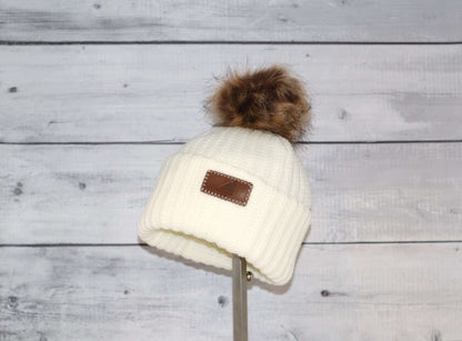 Toddler Acrylic Ribbed Cuff with Pom Hat – Cozy & Purposeful displayed on a stand with a fluffy pom pom.