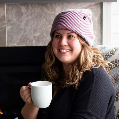 Adult Acrylic Cuff Hat – Soft Knit Beanie worn by a woman holding a mug by a fireplace.