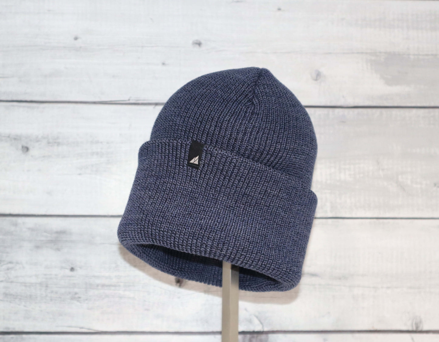 Adult Acrylic Cuff Hat – Soft Knit Beanie displayed on a stand against a wooden background, showcasing its cozy knit design.