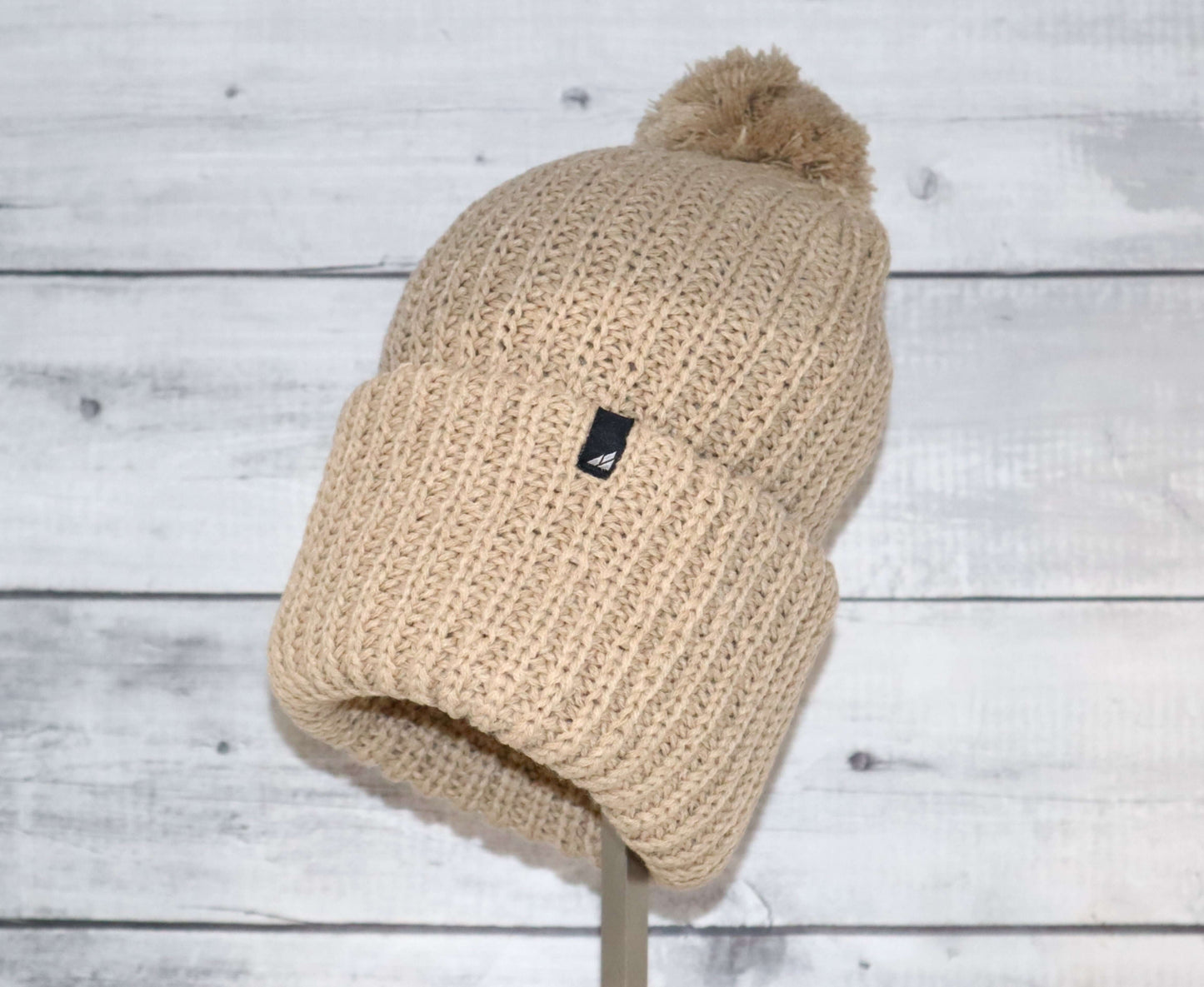 Adult Acrylic Ribbed Cuff Hat with Matching Pom – Cozy & Classic in beige on a display stand.
