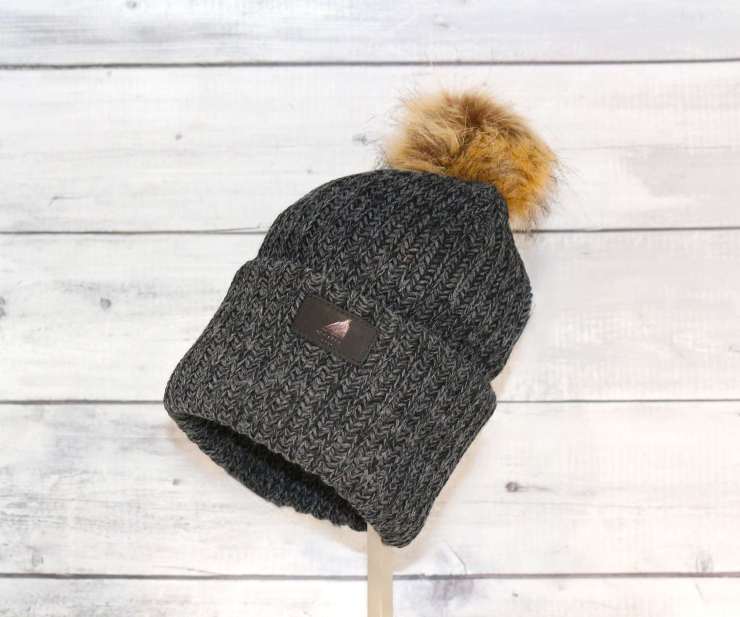 Adult Acrylic Ribbed Cuff with Pom Hat – Cozy, Classic, Giftable displayed on a wooden surface.