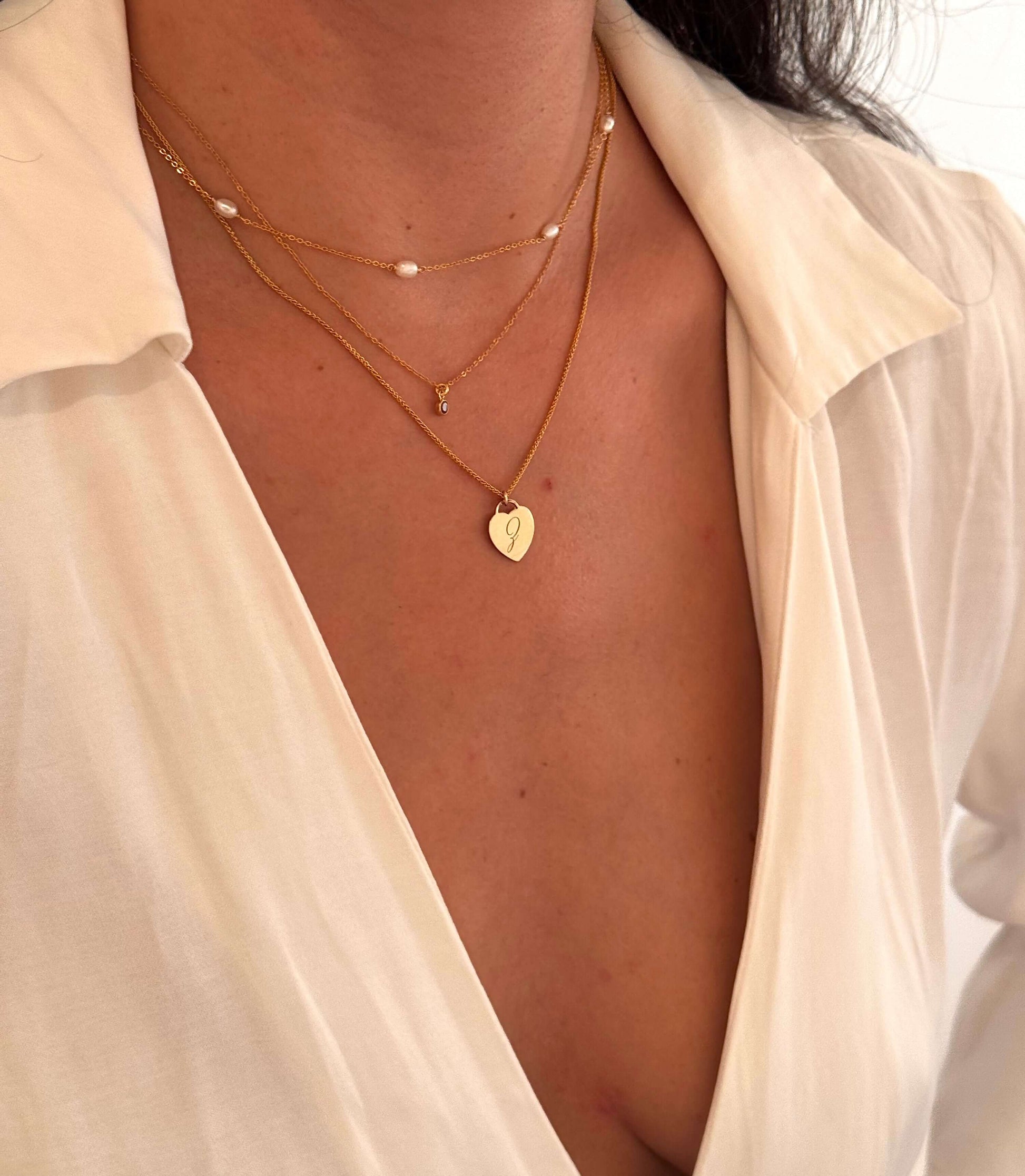 Woman wearing the Alice Initial Necklace – Personalized 14k Gold-Filled Heart layered with other gold necklaces.
