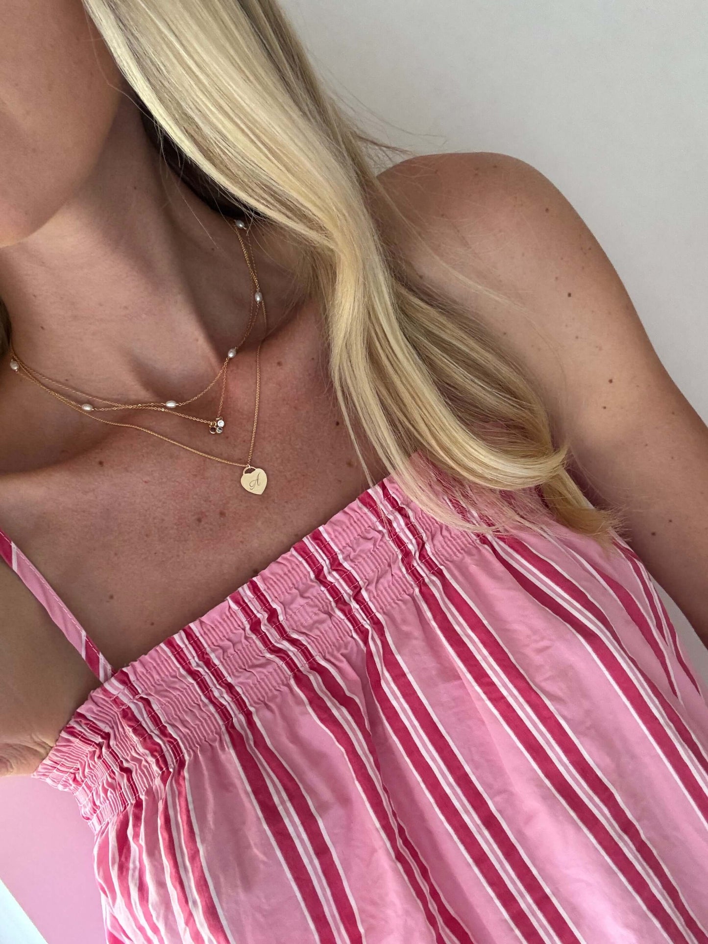 Alice Initial Necklace – Personalized 14k Gold-Filled Heart worn with a pink striped top, showcasing its elegant charm.