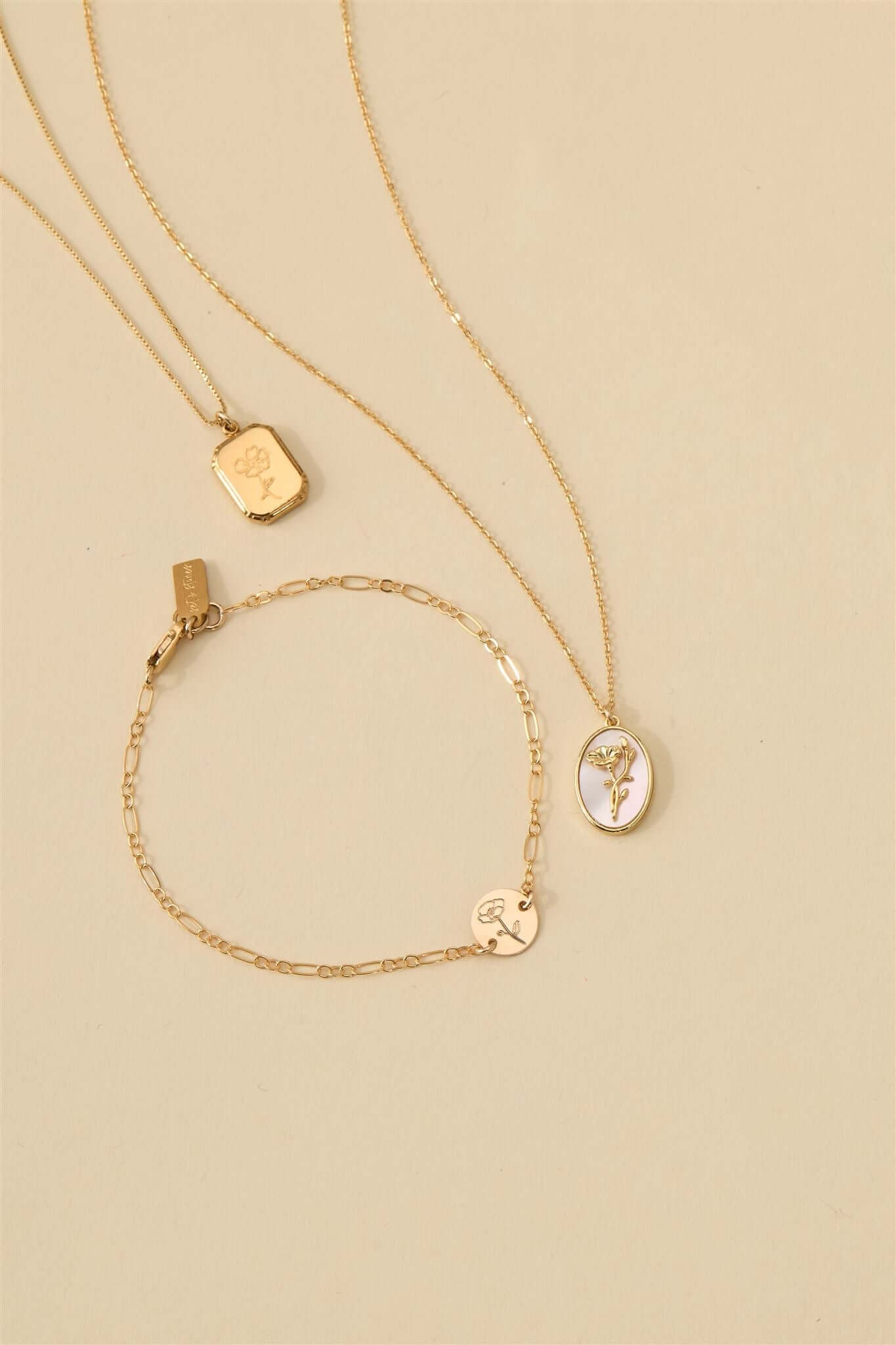 Audrey Birth Flower Necklace – Engraved 18k Gold Over Brass with additional gold jewelry on a soft background.