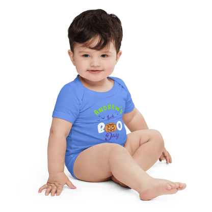 Baby in blue Halloween bodysuit with playful pumpkin design, celebrating 1st Boo Day.