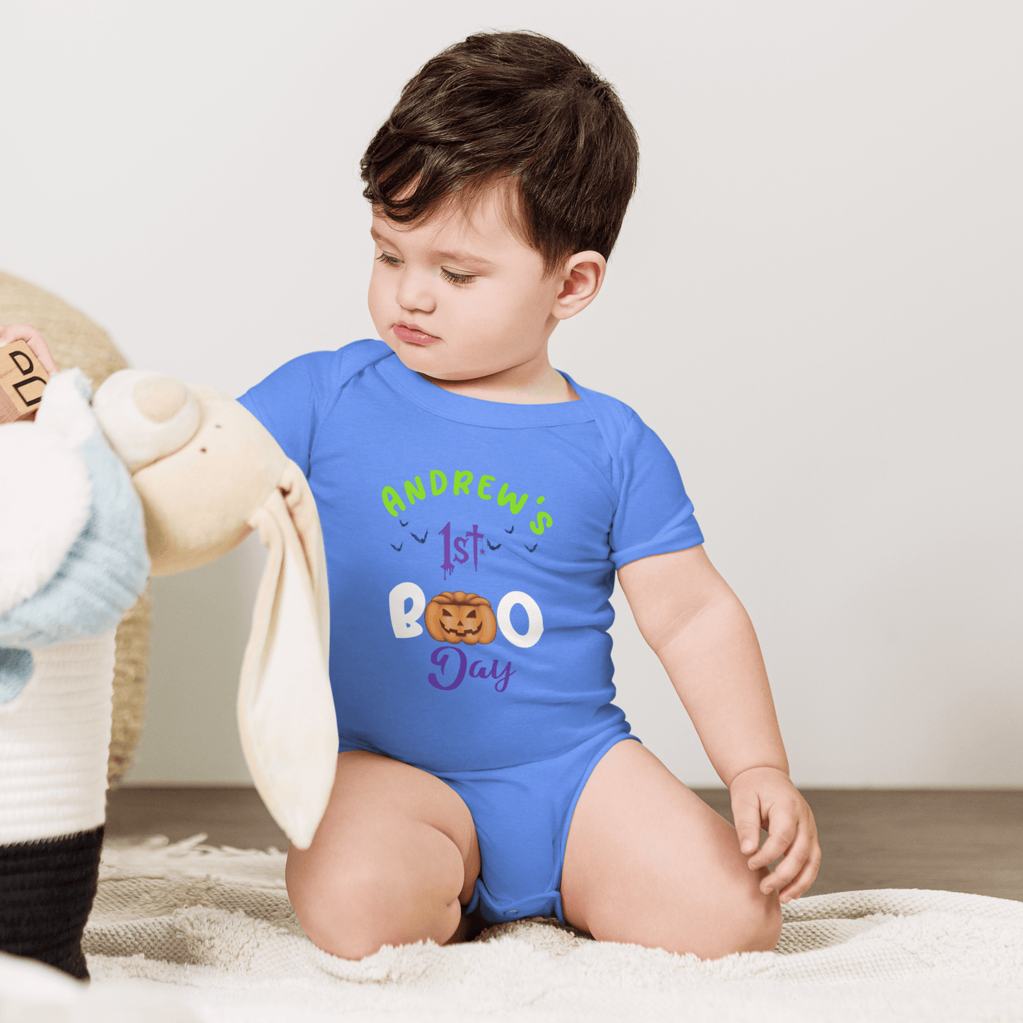 Personalized blue baby bodysuit with 'Andrew's 1st BOO Day' text, featuring pumpkin design for Halloween celebration.