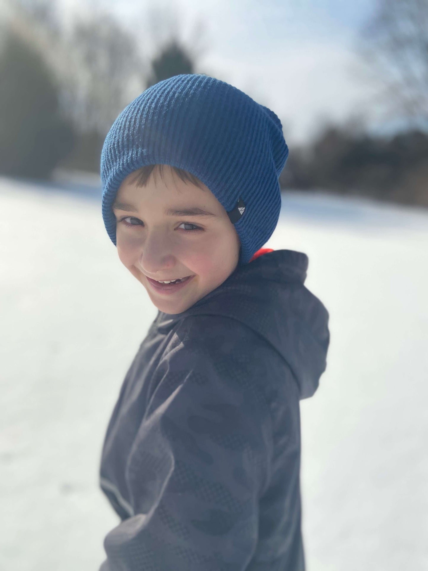 Child Acrylic Cuff Hat – Soft Knit Beanie for Kids worn by a smiling boy in a snowy landscape.