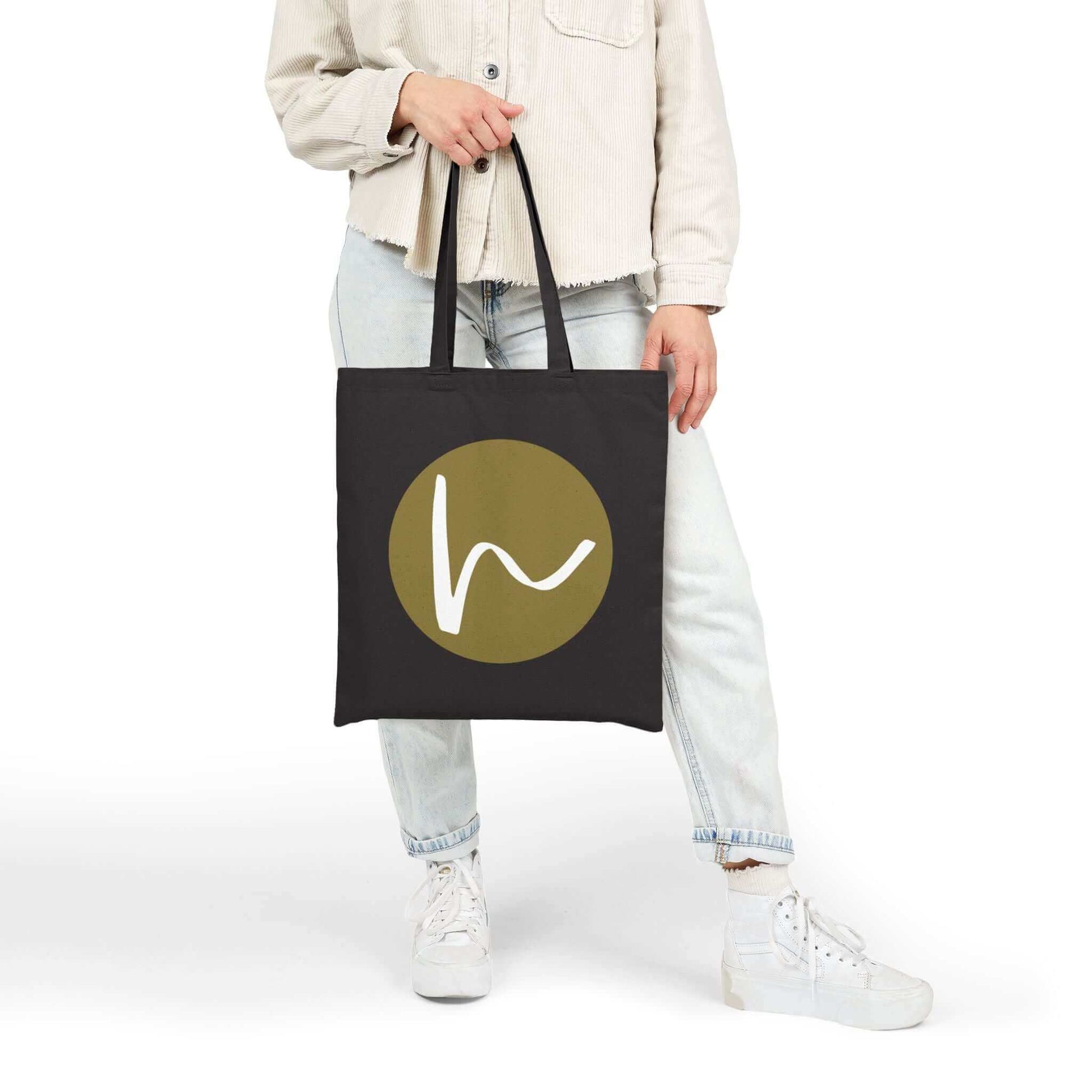 Custom Cotton Canvas Tote Bag – Upload Your Own Design held by a person with a stylish logo on a black background.