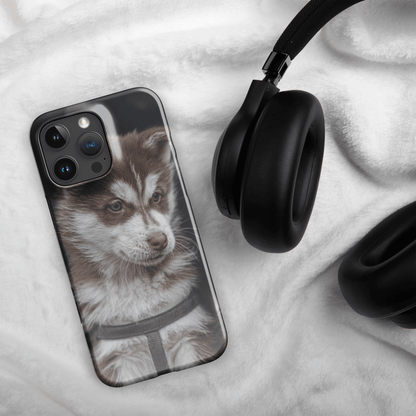 Custom iPhone case featuring a cute husky puppy design, placed next to black headphones on a soft fabric