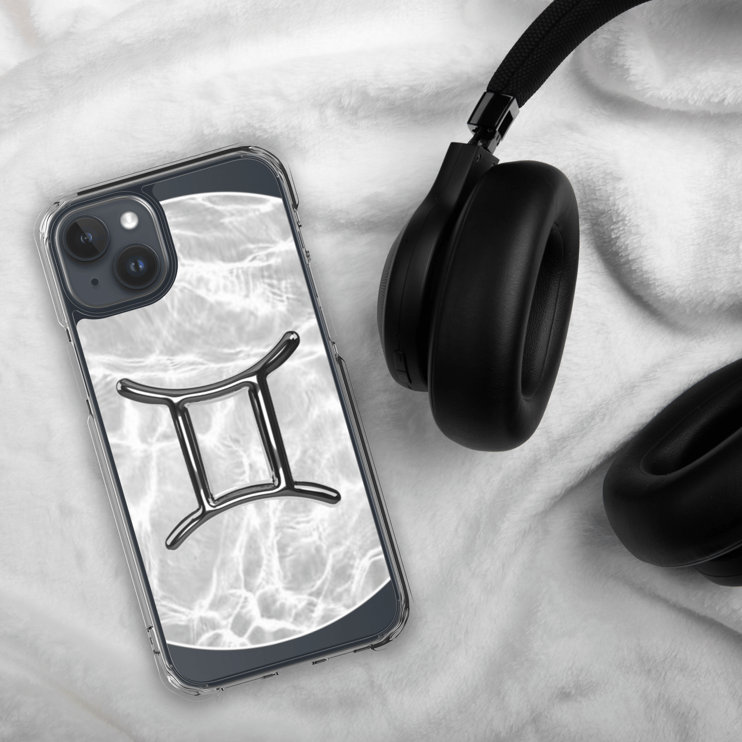 Clear iPhone case featuring Gemini zodiac design on a marble backdrop, paired with stylish headphones.