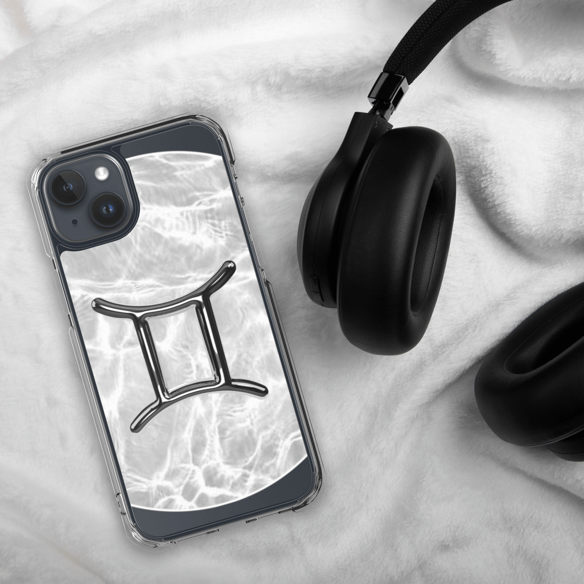 Clear iPhone case featuring Gemini zodiac design on a marble backdrop, paired with stylish headphones.