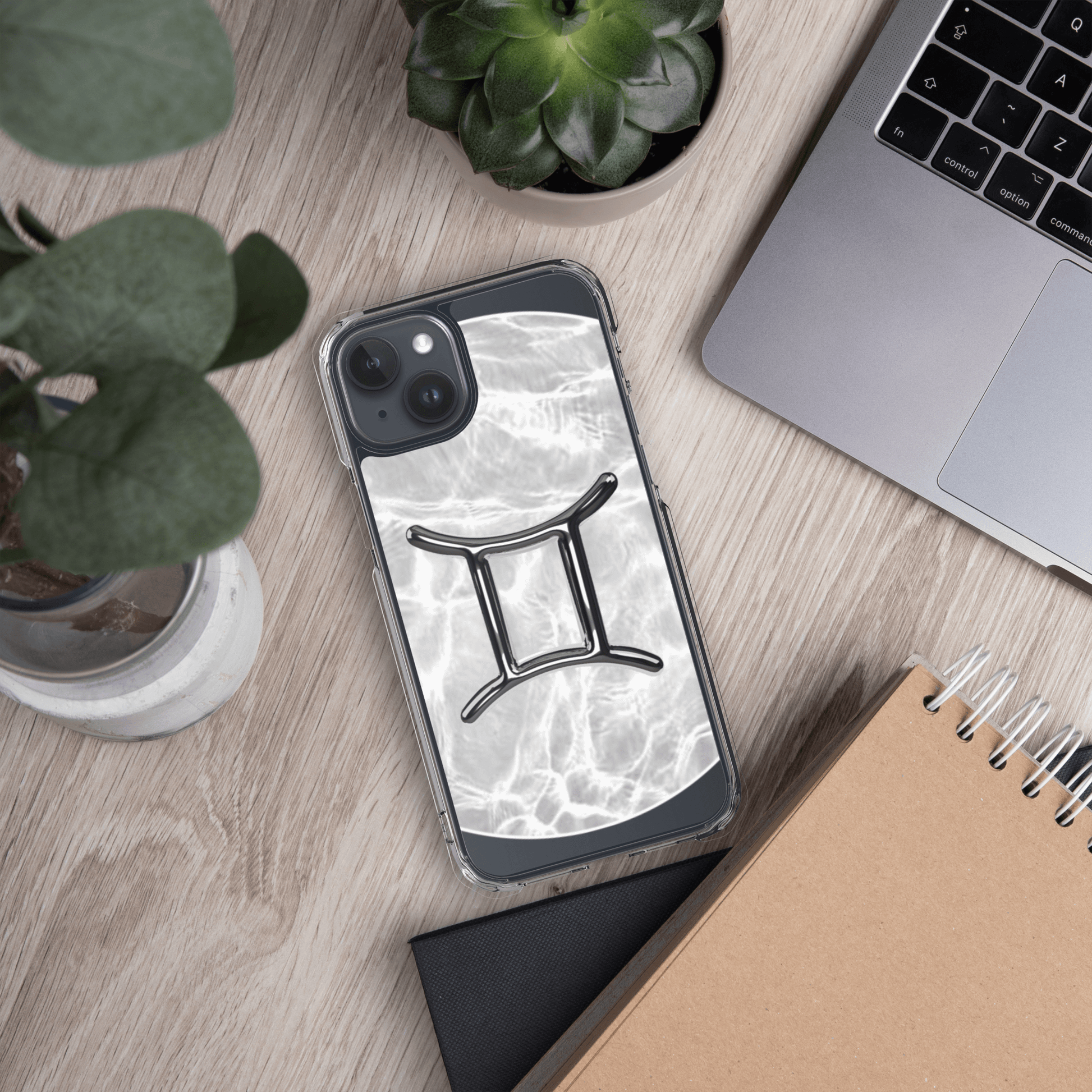 Zodiac Gemini MagSafe clear iPhone case with marble metallic design on a wooden desk alongside plants and a laptop.