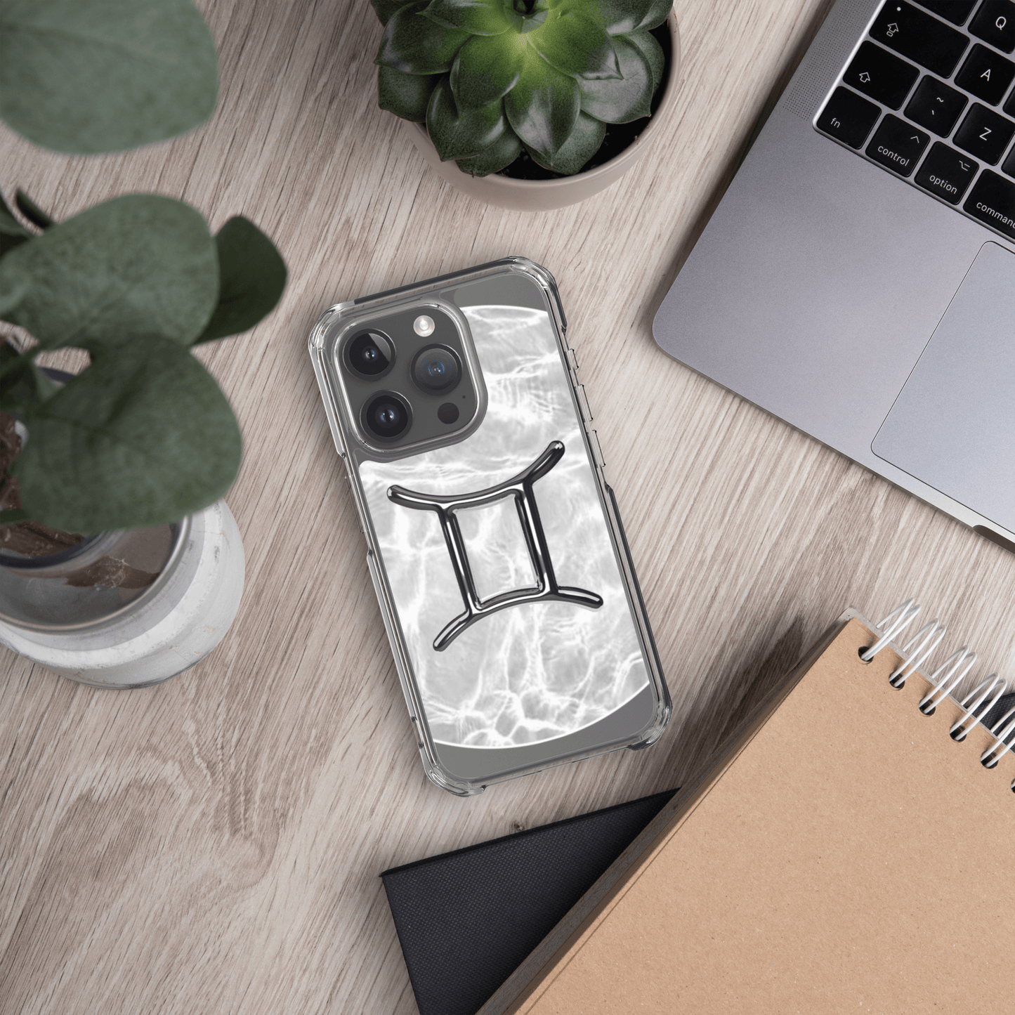 Zodiac Gemini Magsafe clear iPhone case with marble metallic design on a desk with plants and laptop.