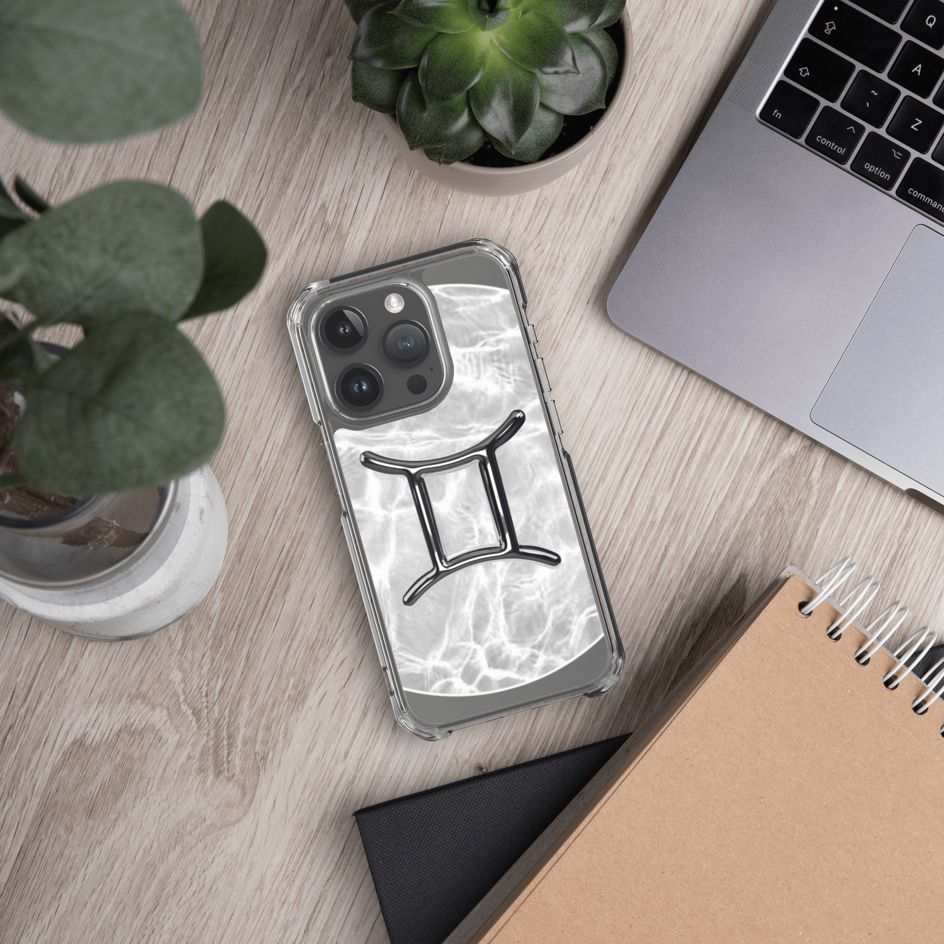 Zodiac Gemini Magsafe clear iPhone case with marble metallic design on a desk with plants and laptop.