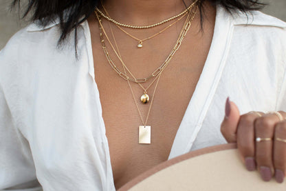 Goldie MAMA Necklace – Hand-Stamped 14k Gold-Filled Pendant layered with other gold necklaces on a model.