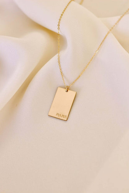 Goldie MAMA Necklace – Hand-Stamped 14k Gold-Filled Pendant featuring a minimalist design on a soft fabric background.