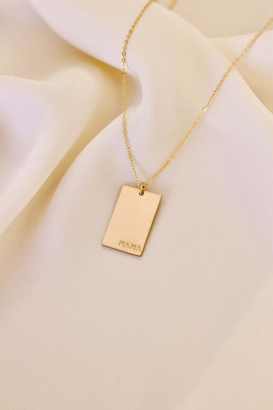 Goldie MAMA Necklace – Hand-Stamped 14k Gold-Filled Pendant featuring a minimalist design on a soft fabric background.