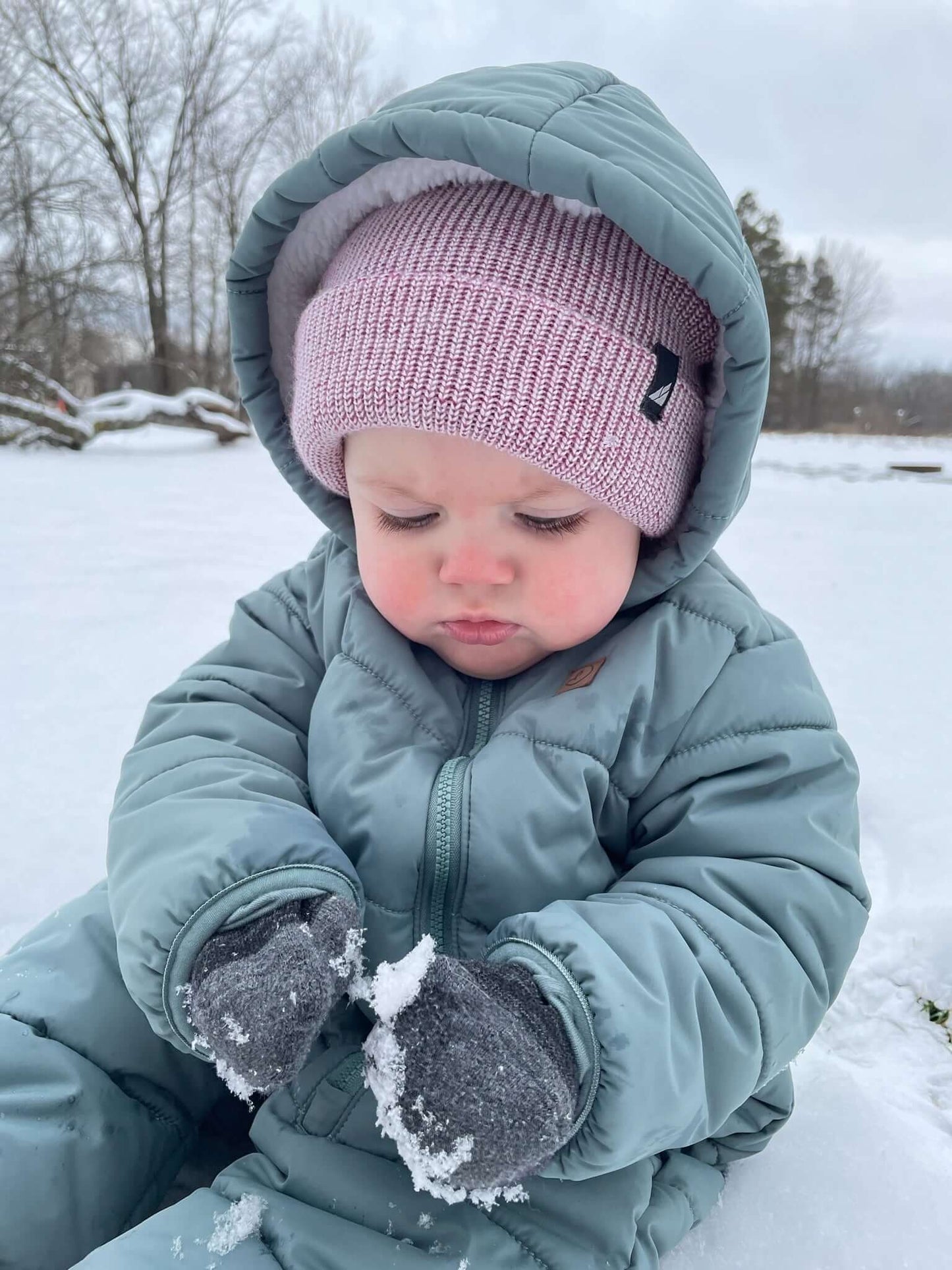 Infant Acrylic Cuff Hat – Soft Knit Beanie for Ages 3–12M worn by a baby playing in the snow, dressed in a warm winter suit.
