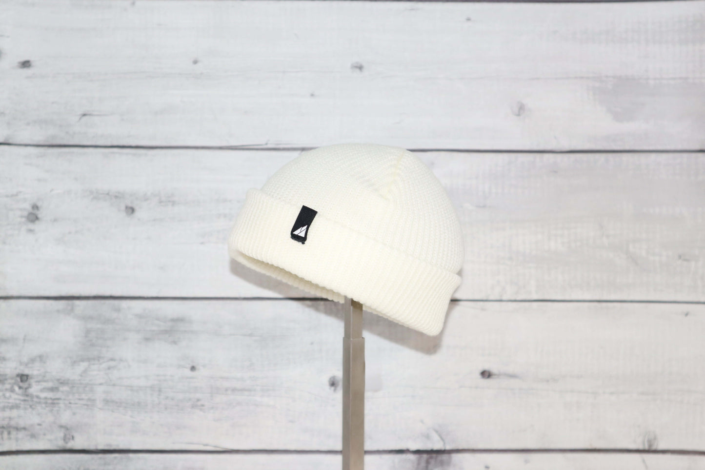 Infant Acrylic Cuff Hat – Soft Knit Beanie for Ages 3–12M displayed on a stand against a wooden backdrop.