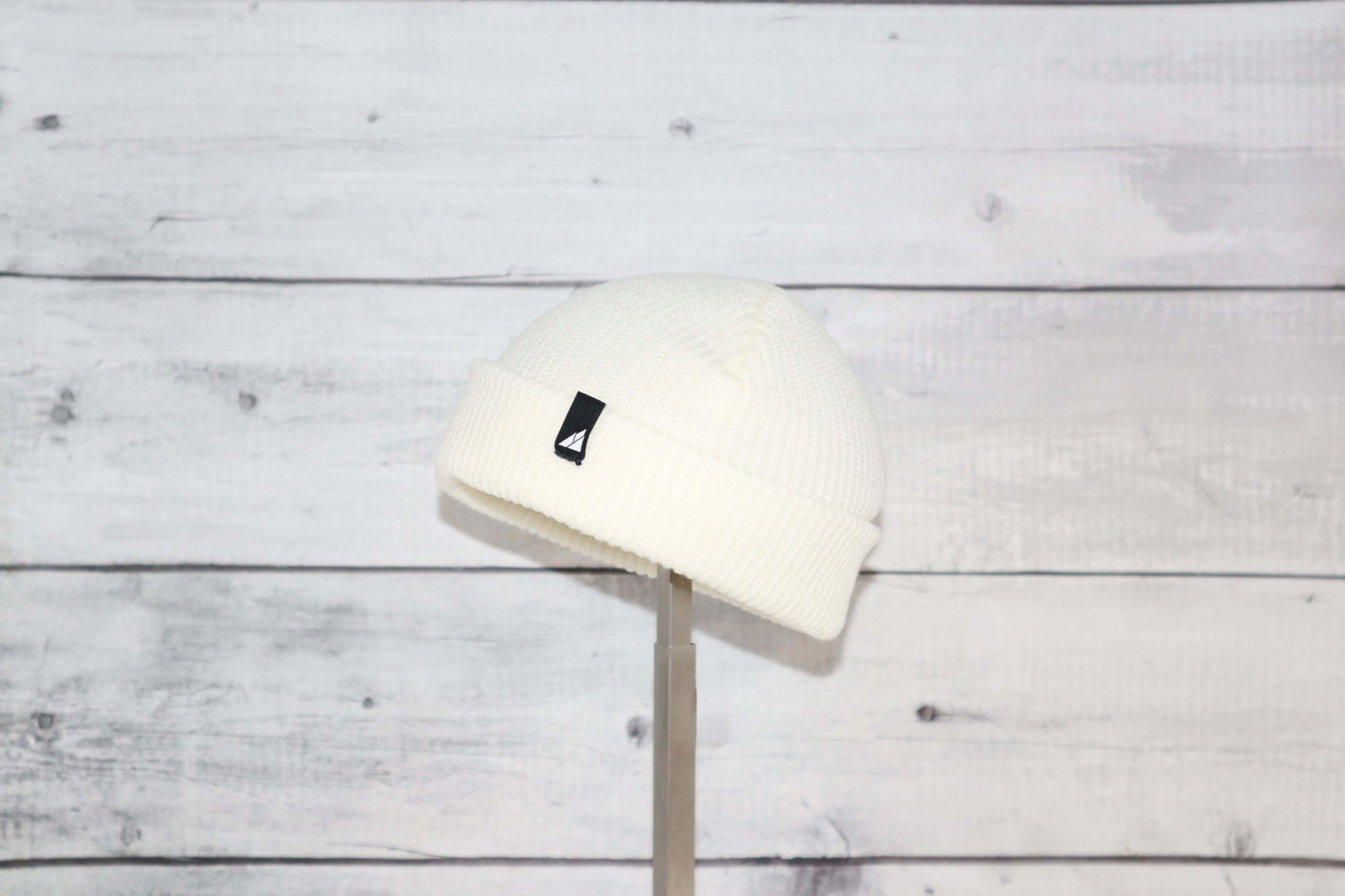 Infant Acrylic Cuff Hat – Soft Knit Beanie for Ages 3–12M displayed on a stand against a wooden backdrop.