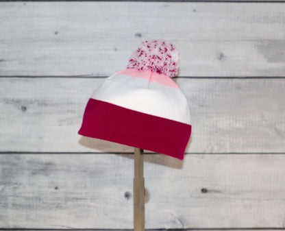 Infant Specialty Hat – Cozy, Playful, Purposeful with white and pink stripes and a pom pom on top.