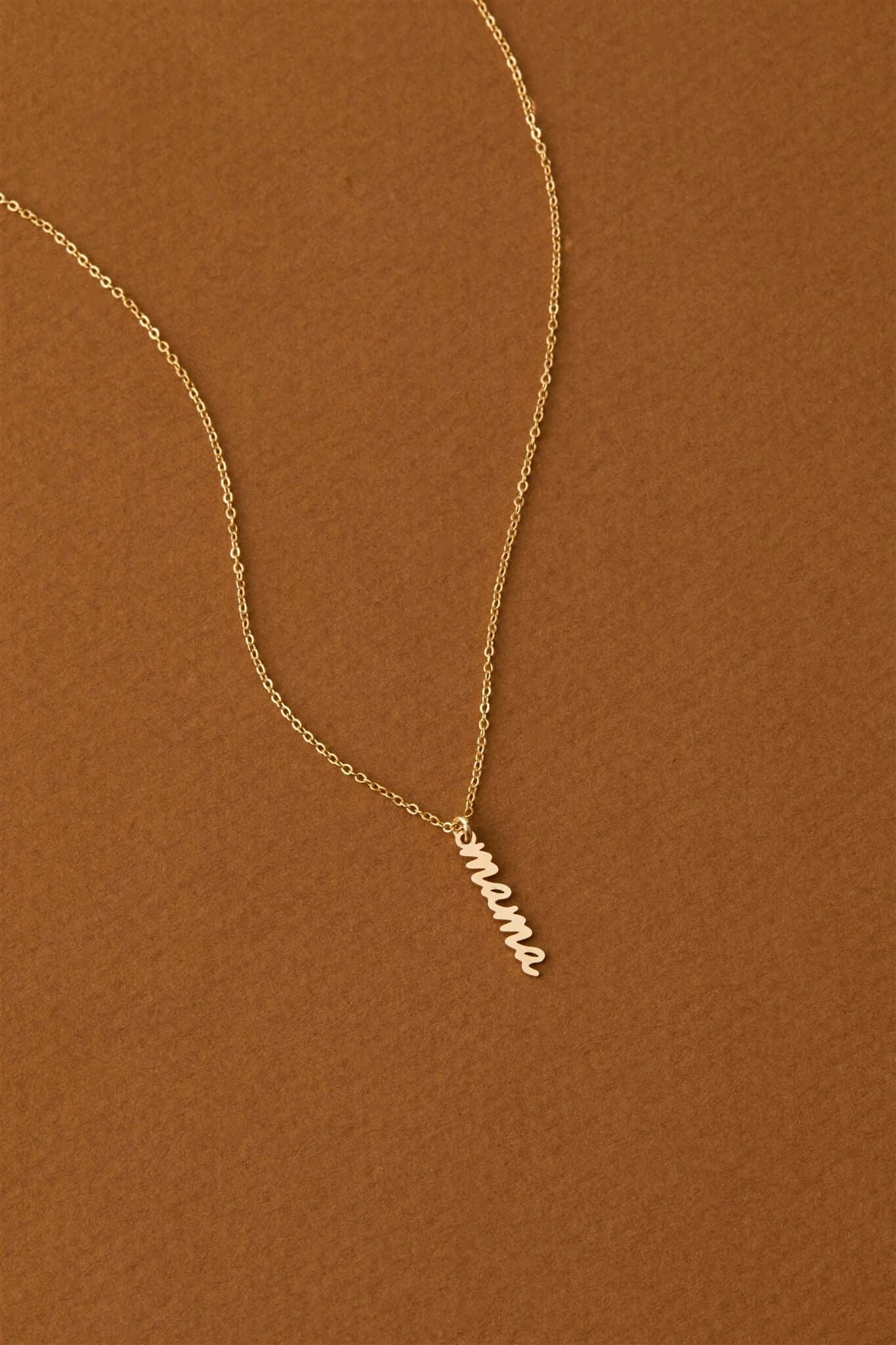 Mama Charm Necklace – 14k Gold-Filled Chain & Pendant on a warm brown background, highlighting its elegant design.