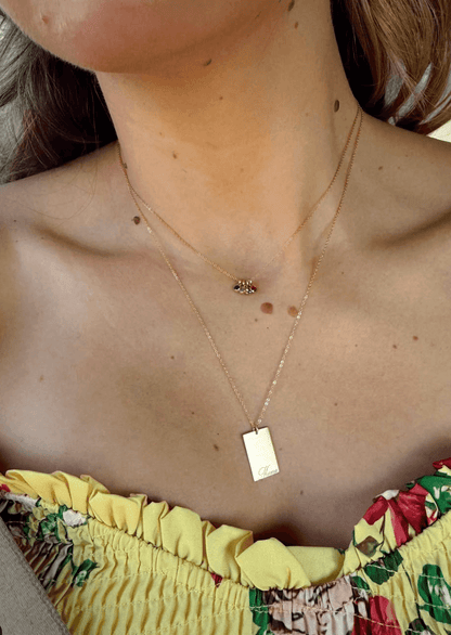 Mama Stella Necklace – 14k Gold-Filled Hand-Engraved Pendant worn with layered necklaces on a woman in a yellow floral top.