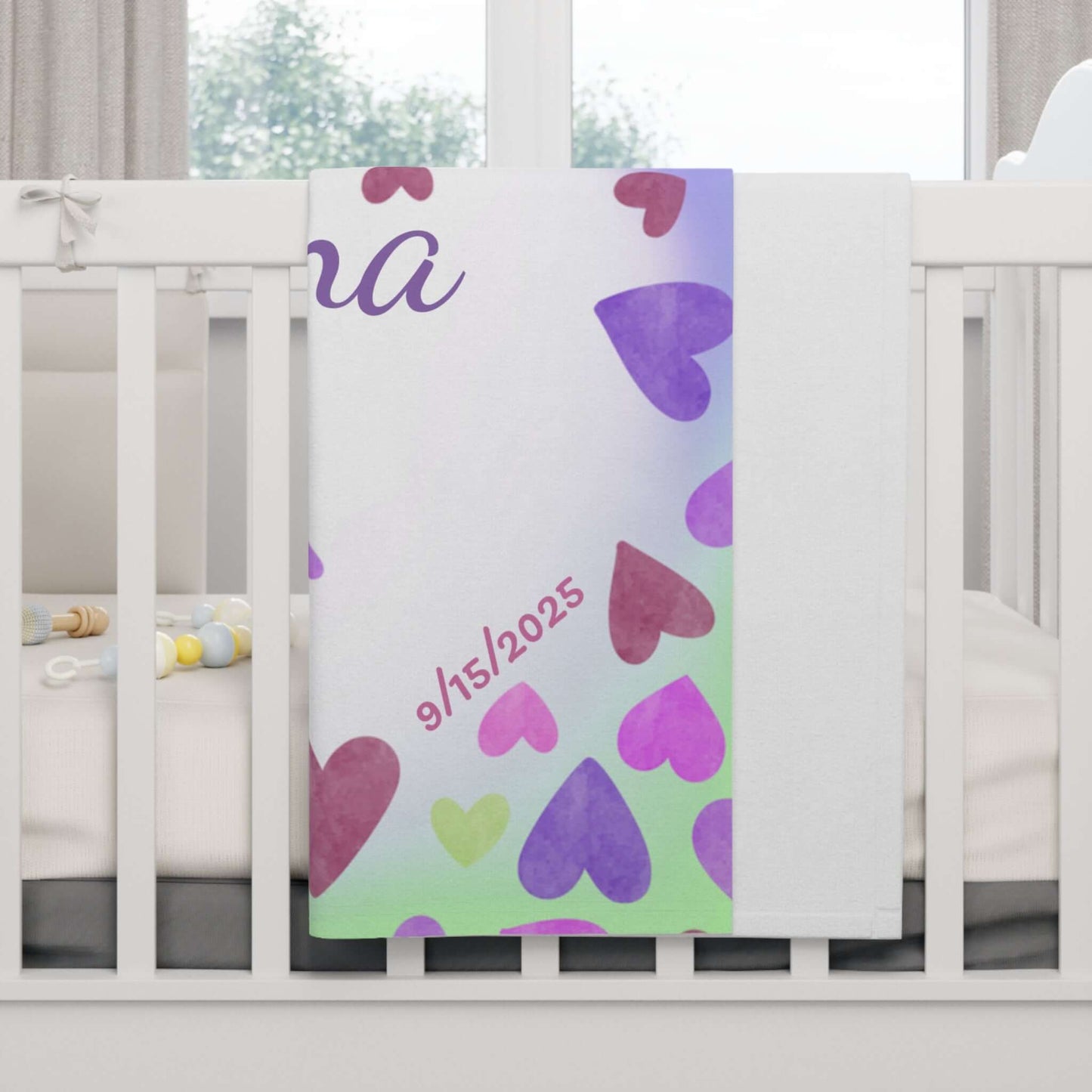 Personalized baby blanket with heart-themed design featuring name and date in a crib.