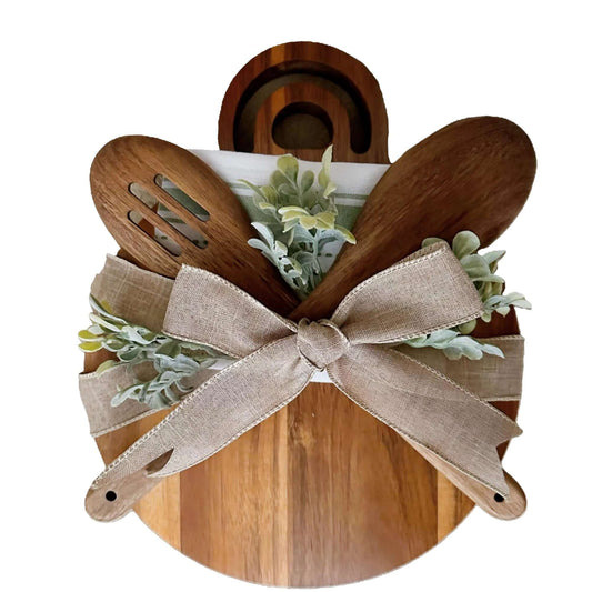 Wooden cheese board gift set with utensils, greenery, and a decorative ribbon, perfect for entertaining.